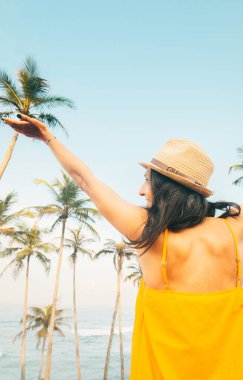 Genç kaygısız mutlu kadın gezgin sarı yazlık elbiseler giyer hasır şapka giyer tropik tatil yerlerinde Palm Beach 'in tadını çıkarır. Turizm turu kaygısız tatil atmosferi tropik seyahat tatili