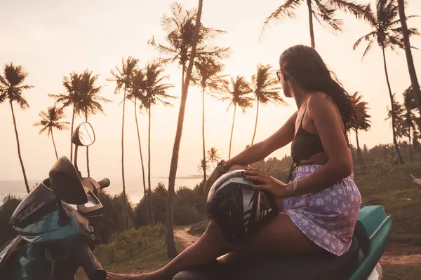 Güneydoğu Asya 'da Sri Lanka' da tek başına seyahat eden güzel genç bir kadın tropikal günbatımında skuterin üzerinde oturuyor.
