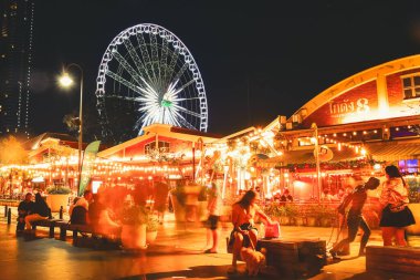 Bangkok, Tayland, 15 Şubat 2024: Bangkok, Tayland 'daki Asiatique The Riverfront' ta renkli gece manzarası, parlayan ışıklar, dönme dolap, hareketli ziyaretçiler ve nehir kenarındaki depo tarzı dükkanlar