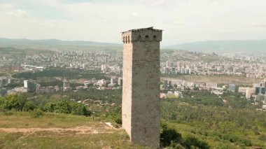 Hava panoramik manzarası Tiflis ufuk çizgisi ve Kaplumbağa Gölü üzerindeki antik Svan taş kulesi, Kafkas savunma mirasını, geleneksel mimariyi ve tarihi muhafazayı sembolize ediyor.