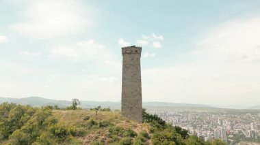 Hava panoramik manzarası Tiflis ufuk çizgisi ve Kaplumbağa Gölü üzerindeki antik Svan taş kulesi, Kafkas savunma mirasını, geleneksel mimariyi ve tarihi muhafazayı sembolize ediyor.