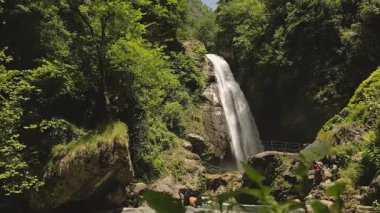 Lahodekhi, Gürcistan - 11 Mayıs 2025: Hava manzaralı turist ve Ninoskhevi Şelalesi yemyeşil bir ormanın içinden geçerek Gürcistan 'ın Lagodekhi Korunan Bölgeleri' nde yer alan kayalık bir havuza dökülüyor.