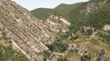 Hava manzaralı turist yürüyüşçüleri, Mtskheta, Gürcistan yakınlarındaki önemli antik savunma sisteminin bir parçası olan eğimli kaya oluşumları ve orman tepeleri ile dik yamaçlardaki Armazi Kalesi 'ni gezmeyi keşfederler.