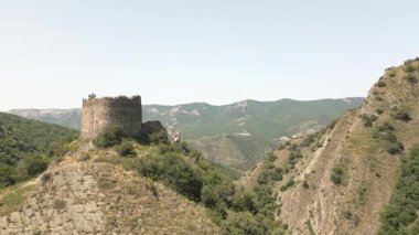 Hava manzaralı turist yürüyüşçüleri, Mtskheta, Gürcistan yakınlarındaki önemli antik savunma sisteminin bir parçası olan eğimli kaya oluşumları ve orman tepeleri ile dik yamaçlardaki Armazi Kalesi 'ni gezmeyi keşfederler.