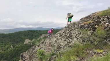 Havadan zum yaparak uzaklaşan iki yetişkin çift tepenin zirvesine ulaştılar ve verimli yeşil orman ve dramatik yaz manzarasıyla çevrili sarp, kayalık yamaçlarda ekip çalışmasına yardım ettiler.