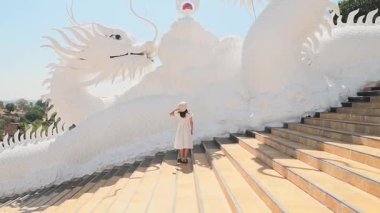 Kadın turistler şık beyaz elbiseler giyip gezerken Tayland 'ın Chiang Rai kentindeki Wat Huay Pla Kang tapınağının merdivenlerinde ikonik beyaz ejderhaları keşfediyor. Meşhur seyahat yeri.