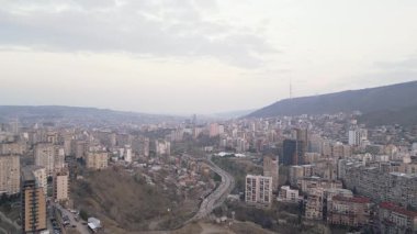 Tiflis başkentinin akşam manzarası Mtantsminda ilçe tepelerini, konut kulelerini ve şehir sokaklarını gösterirken hafif trafik ve açık sonbahar renkleriyle