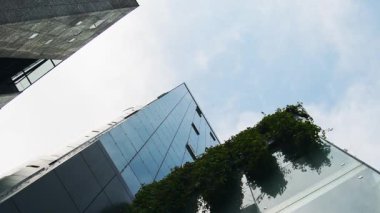 İş alanının yukarı açısı, cam kaplı gökdelen binaları, yeşil cepheli balkon, ekolojik bilinçli kentsel tasarım modern mimari sergileniyor.