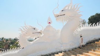 Chiang Rai, Thailand - 2023: Woman tourist wear stylish white dress sightseeing explores iconic twin white dragons on temple stairs at Wat Huay Pla Kang in Chiang Rai, Thailand under clear blue sky