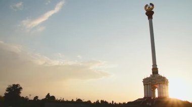Dushanbe, Tacikistan - 2024: Tacikistan Amblemi ile Stele Rudaki Parkı 'ndan gün batımında görülüyor. Ulusal taç, yedi yıldız, buğday, üstünde pamuk sembolleri. Turist ziyareti
