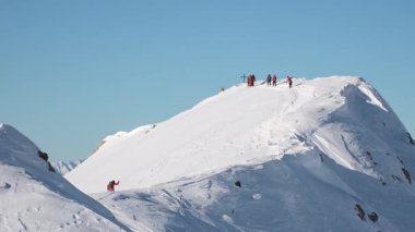 Freeriderlar açık mavi gökyüzü altında karlı yamaçlarda yürüyüşe çıkarak ekstrem kış sporları, macera, risk, taşra keşfi, doğa gücü, takım çalışması, dayanıklılık ve alp özgürlüğünü sembolize ediyor.