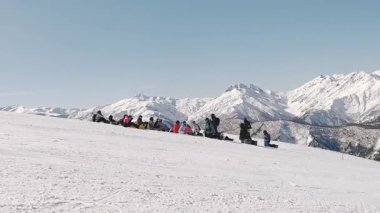 Mestia, Gürcistan - 2025: Genç Snowboard eğitmeni, kış aylarında Kafkas dağlarıyla çevrili kar yamacında oturan yeni başlayanlara ders veriyor.