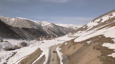Ushguli Gürcistan 'a giden hava manzaralı arazi aracı, Svan kuleleri, ilkbahar karları eridi, Kafkaslar arka planda kaldı. 4x4 araç baharda Ushguli 'ye giden dağ yolunu takip ediyor.