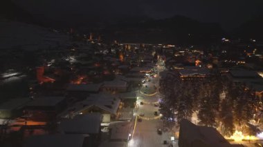 Aydınlanmış Mestia Dağı kayak merkezinin kış aylarında tatil dekorasyonları, karlı çatıları ve şenlikli sokak ambiyansı olan binaları üzerinde gece uçuşları. Popüler kayak gezisi hedefi