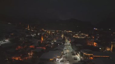 Aydınlanmış Mestia Dağı kayak merkezinin kış aylarında tatil süslemeleri, karlı çatıları ve şenlikli sokak atmosferiyle aydınlatılmış gece hava manzarası. Popüler kayak gezisi hedefi