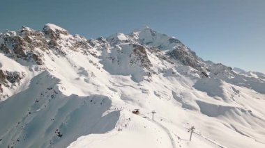 Freeriderlar açık mavi gökyüzü altında karlı yamaçlarda yürüyüşe çıkarak ekstrem kış sporları, macera, risk, taşra keşfi, doğa gücü, takım çalışması, dayanıklılık ve alp özgürlüğünü sembolize ediyor.