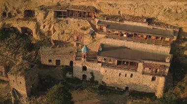 Ortodoks keşiş sohbetinin havadan görüntüsü, uzak mağara manastırı kompleksindeki ziyaretçilerle, Gürcistan 'daki ruhani bağlılığı, izolasyonu ve münzevi yaşam tarzını sembolize eden, uçurumlara oyulmuş bir şekilde konuşuyor.