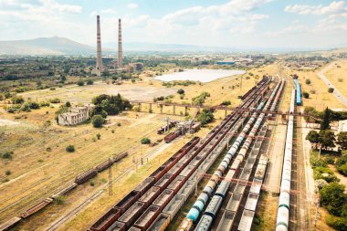 İHA, yük vagonlarını paralel raylarda, endüstriyel lojistiği, ihracat-ithalat akışını ve ulaşım altyapısını sembolize eden yük vagonlarını gösteriyor.