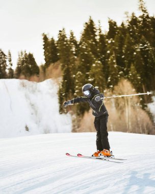 Siyah pantolon giyen genç kayakçı, karlı yamaçlarda serbest stil atlıyor. Orman hilesi, kış ortasında serbest sürüş, ekstrem spor konsepti.