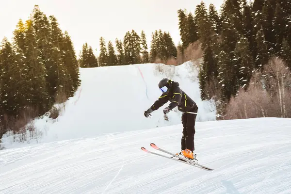 Siyah pantolon giyen genç kayakçı, karlı yamaçlarda serbest stil atlıyor. Orman hilesi, kış ortasında serbest sürüş, ekstrem spor konsepti.