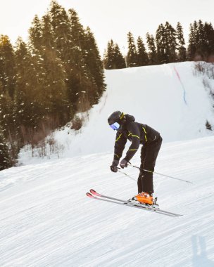 Siyah pantolon giyen genç kayakçı, karlı yamaçlarda serbest stil atlıyor. Orman hilesi, kış ortasında serbest sürüş, ekstrem spor konsepti.