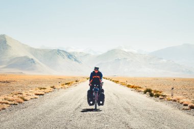 Pamir 'in uzak yüksek dağlarındaki Pamir otoyolu M41 yolunda tek başına turlayan maceracı beyaz erkek bisiklet. Pamir otoyolu macera rotası
