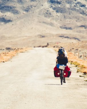 Arkadan bakıldığında maceracı beyaz erkek bisiklet, Pamir 'in uzak dağlarında Pamir otoyolu M41 yolunda tek başına turluyor. Pamir otoyolu macera rotası
