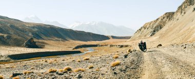 Dört pannier çantasına yüklenmiş kırmızı bisiklet. Çakıl yolunun kenarında duruyor. Etrafı vahşi Pamir dağlarıyla çevrili. Yalnız macera seyahati