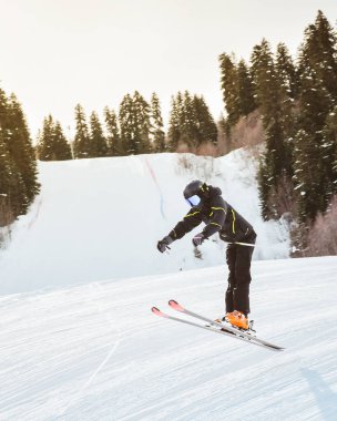 Siyah pantolon giyen genç kayakçı, karlı yamaçlarda serbest stil atlıyor. Orman hilesi, kış ortasında serbest sürüş, ekstrem spor konsepti.