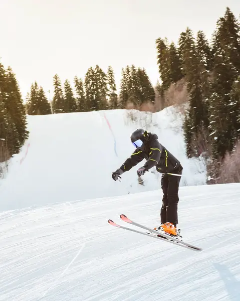 Siyah pantolon giyen genç kayakçı, karlı yamaçlarda serbest stil atlıyor. Orman hilesi, kış ortasında serbest sürüş, ekstrem spor konsepti.