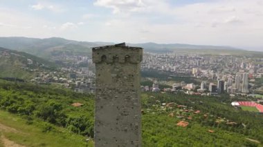 Tiflis ufuk çizgisi ve Kaplumbağa Gölü üzerindeki antik Svan taş kulesi etrafındaki hava çemberi, Kafkas savunma mirasını, geleneksel mimariyi ve tarihsel korumayı sembolize ediyor.