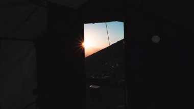Ararat Dağı ana kampının çadır girişinden gün doğumu ışınları, Türkiye 'nin engebeli volkanik arazisindeki kampa tırmanıyor.