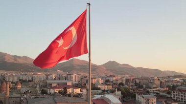 Dev Türk bayrağı -hilal ve yıldız- gün batımında bir Anadolu şehrinin üzerinde dalgalanır, ufukta dağlar - ilham verici, vatansever bir manzara