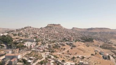 Türkiye 'nin güneydoğusundaki Mardin kentinin havadan hızlı görüntüsü, tepede kale, dik yamaçta taş evler, kurak Mezopotamya manzarası. Geleneksel bej kireçtaşı evler ve tarihi yapılar.