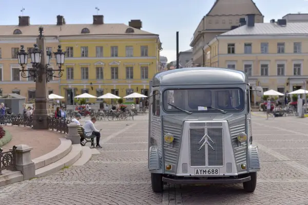 stock image Vintage Citroen H Van parked in a cobblestone square in Helsinki, surrounded by historic yellow buildings and outdoor cafes with patrons enjoying the ambiance.