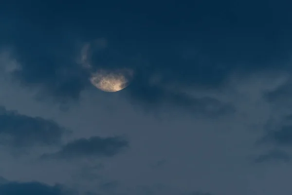Growing moon in clouds on evening sky