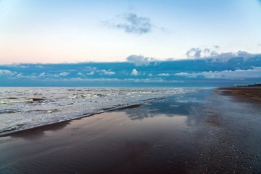Gün batımından sonra kumlu okyanus kıyısı. Uzakta kara bulutlar var.