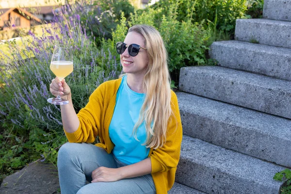 黄色のセーターを着た若い笑顔の女性がワインを片手に座っている — ストック写真