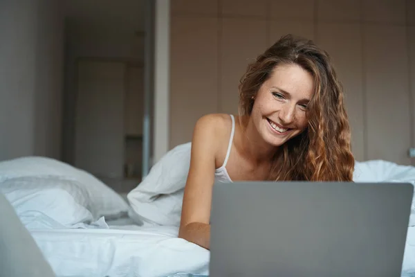 快乐的女士在醒来后用笔记本电脑 脸上挂着快乐的笑容 — 图库照片