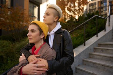 Sarı şapkalı esmer kız arkadaşının kollarında, kız arkadaşları sonbahar manzarasının arka planında merdivenlerde dikiliyor.