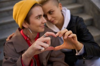 Genç LGBT kadın çifti kalp şeklinde el ele tutuşurken, kadınlar merdivenlere yerleşti.