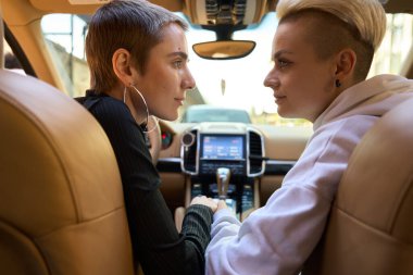 Dişi LGBT çifti güzel bir arabada oturur, kadınlar birbirlerinin gözlerinin içine bakar ve el ele tutuşurlar.