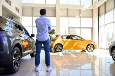 Otomotiv bayiliğinde yepyeni lüks arabaların arasında duran adamın arka planı