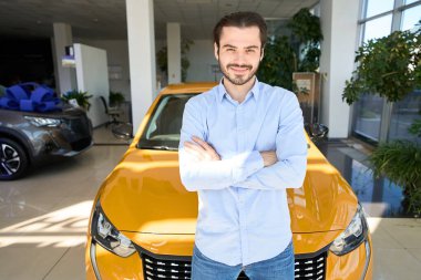 Gülümseyen genç adam yeni lüks arabanın önünde kameraya poz veriyor.