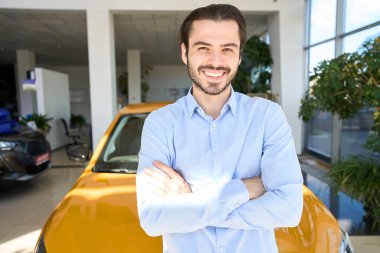 Lüks bir arabanın önünde durup geleceğe bakan neşeli bir araba galerisi müşterisi.