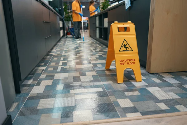Warning sign Attention wet floor stands indoors on the floor, the cleaner washes the floor with a mop