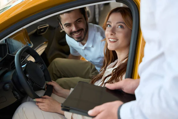 笑顔の若い女性と男が自動車に座って営業担当者を見て — ストック写真
