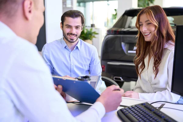 Przedstawiciel Handlowy Auto Pokazujący Umowę Zakupu Uśmiechniętemu Młodzieńcowi Jego Towarzyszce — Zdjęcie stockowe