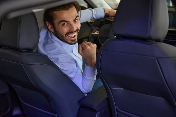 笑顔幸せな若い男の後ろに座ってステアリングホイールの真新しい車 — ストック写真