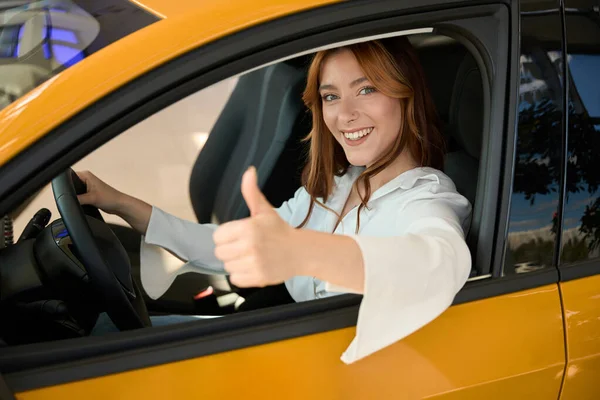兴高采烈的女司机坐在汽车方向盘后面 竖起大拇指标志 — 图库照片